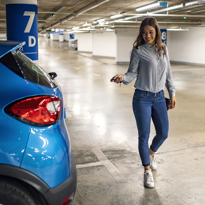 Frau steht neben ihrem Auto in einer Tiefgarage und schließt ihr Auto auf