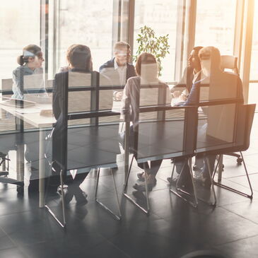 Sieben Personen sitzen an einem Tisch im Meeting-Raum