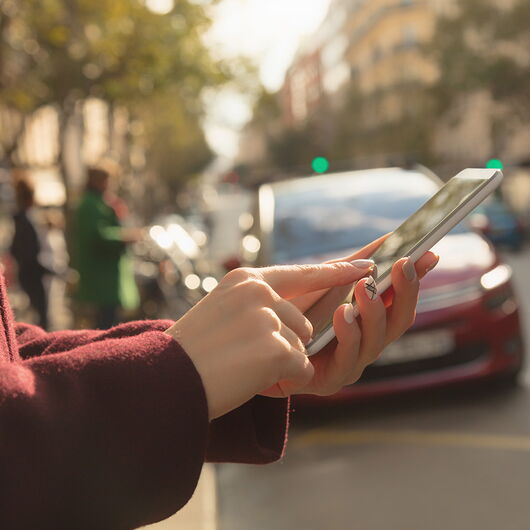Frau steht am Straßenrand und tippt in ihr Smartphone